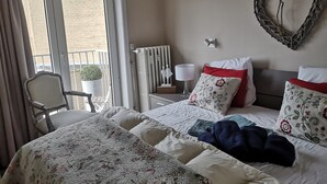 Una camera d'albergo con un letto, una sedia, un termosifone, una decorazione a forma di cuore appesa al muro e vista sull'esterno.