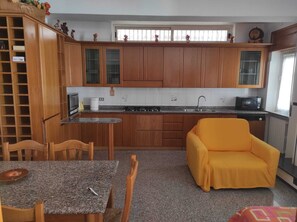 Uma cozinha compacta com armários de madeira, uma mesa de jantar, cadeiras, um sofá pequeno e um micro-ondas.