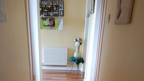 A hallway with wooden flooring, a radiator, and a small table with a vase of flowers. - Room in Bungalow - Very Nice View With This Room (Sneem)