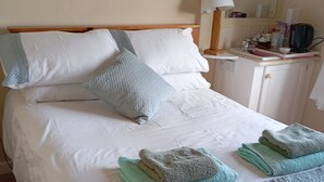 A neatly made bed with white and light blue bedding, a wooden headboard, and a bedside table with a lamp and a small cabinet. - Room in Bungalow - Very Nice View With This Room (Sneem)
