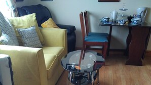 A living room with a yellow sofa, a glass coffee table, a wooden chair, and a black furry rug. - Room in Bungalow - Very Nice View With This Room (Sneem)