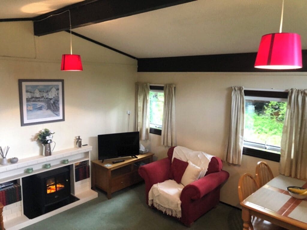 A cozy living room with a fireplace, a red armchair, a television, and a dining table.