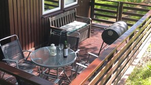 A deck with a round glass table, two chairs, a bench, and a grill. - Nuthatch Lodge is set in 24 Acres of Wood, Parkland Near the Village of Cenarth (Newcastle Emlyn)