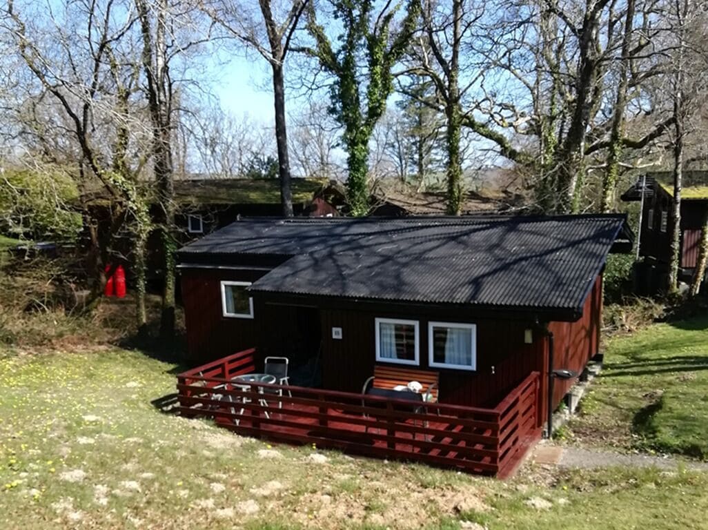 A wooden cabin with a metal roof, a fenced deck, and a small porch.