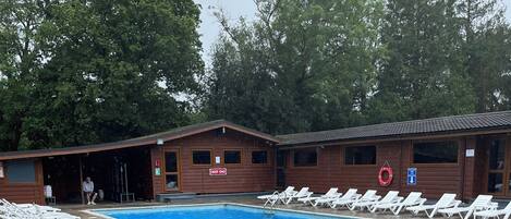 A swimming pool area with lounge chairs, a wooden building with a 'DEEP END' sign, and a lifebuoy.