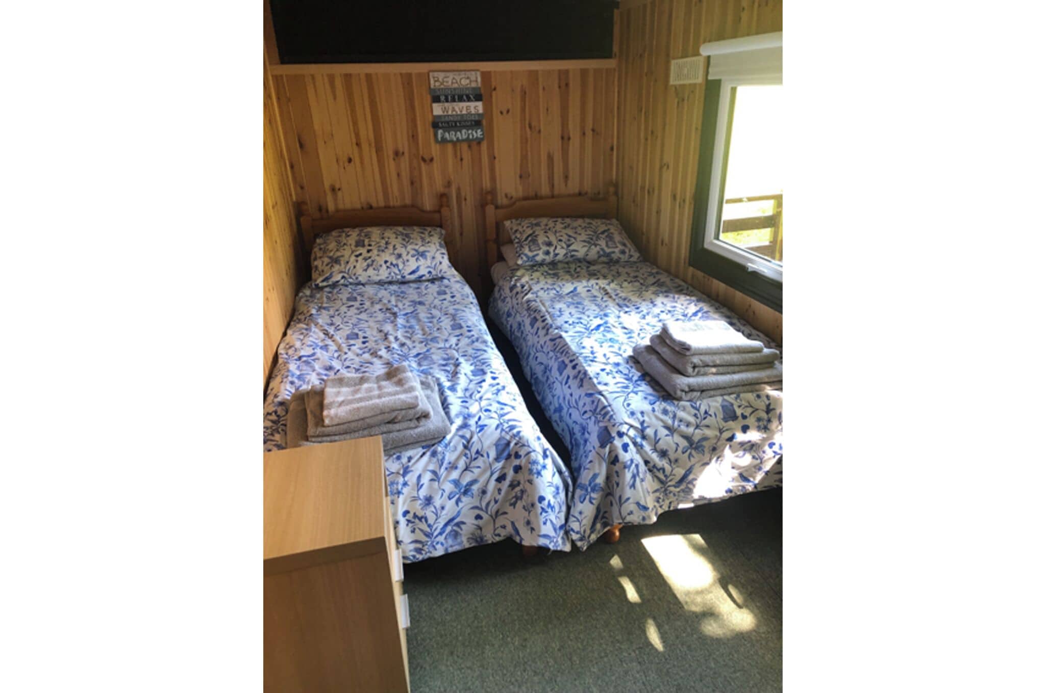 A cabin with two wooden beds, each with floral bedding and towels.