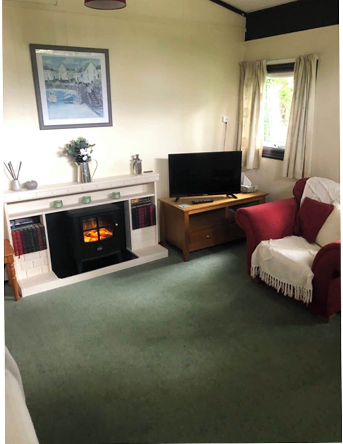 Una sala de estar con chimenea, un televisor sobre un mueble de madera, un sofá rojo y una ventana con cortinas.