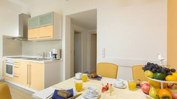 A modern kitchen with a dining area, featuring a breakfast setup with fruits, pastries, and beverages.
