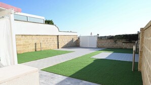 A rooftop patio with artificial grass, a white building, stone walls, and a gated entrance. - Villa Noire 'just 900mt From The Crystalline Waters Of Salento (Nardò)