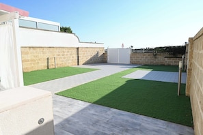 Une terrasse sur le toit avec un revêtement d’herbe artificielle, un bâtiment blanc, des murs en pierre et une entrée fermée par un portail.