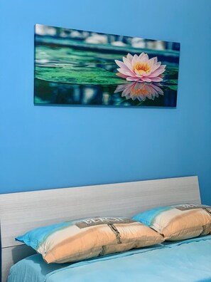 A bedroom with a bed, pillows, and a wall-mounted painting of a water lily.