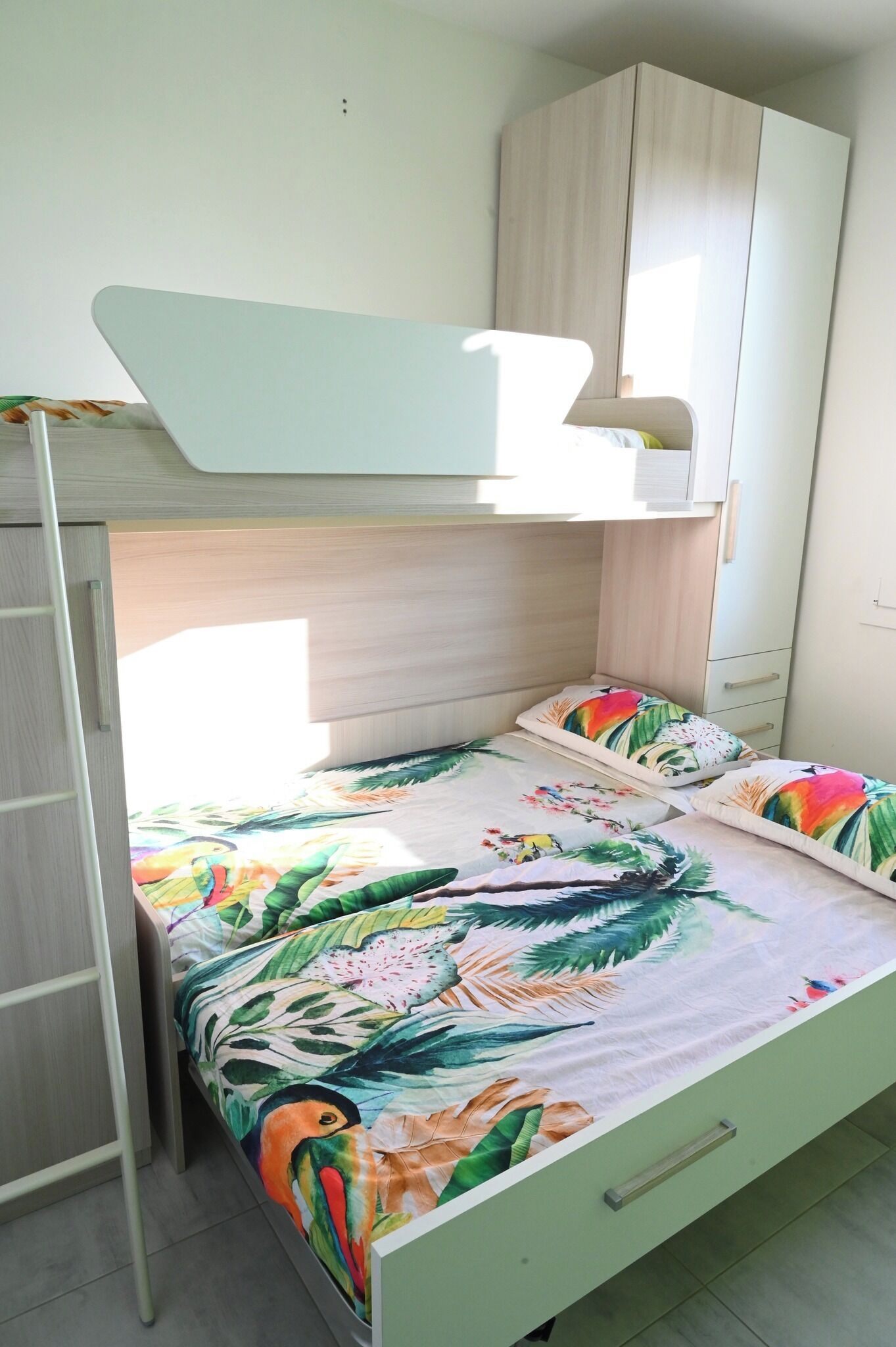 Ein Stockbett mit tropischem Muster, ein Kleiderschrank und eine steile Treppe.