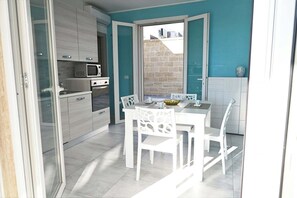 A modern kitchen with white cabinetry, a microwave, and a dining area with white chairs and a table.