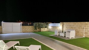 An outdoor patio with artificial grass, white furniture, and a stone wall. - Villa Noire 'just 900mt From The Crystalline Waters Of Salento (Nardò)