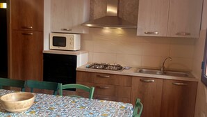 A kitchen with wooden cabinets, a microwave, a gas stove, and a sink. - Villetta Singola a 20metri dal Mare per Soggiorni - Cure Termali Vicino Taormina (Ali Terme)