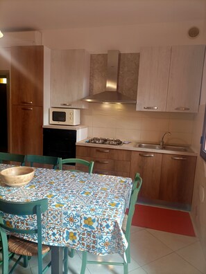 A kitchen with wooden cabinets, a microwave, a gas stove, and a sink. - Villetta Singola a 20metri dal Mare per Soggiorni - Cure Termali Vicino Taormina (Ali Terme)