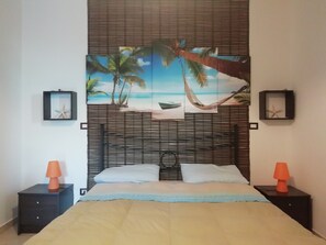 A bedroom with a bed, two nightstands, a headboard with a beach-themed mural, and two framed starfish decorations.