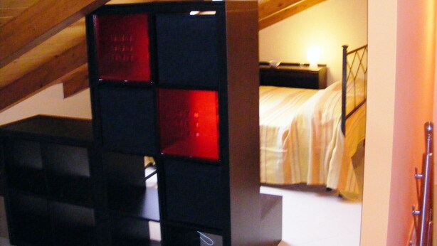 A bedroom with a sloped ceiling, a bed with a headboard, and a nightstand.