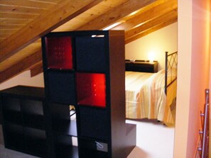 A bedroom with a sloped ceiling, a bed with a headboard, and a nightstand.
