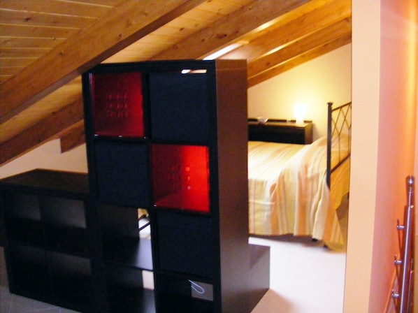 A bedroom with a sloped ceiling, a bed with a headboard, and a nightstand.