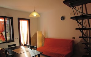 A dining area with a table and chairs, a sofa, a lamp, a clock, and a staircase.