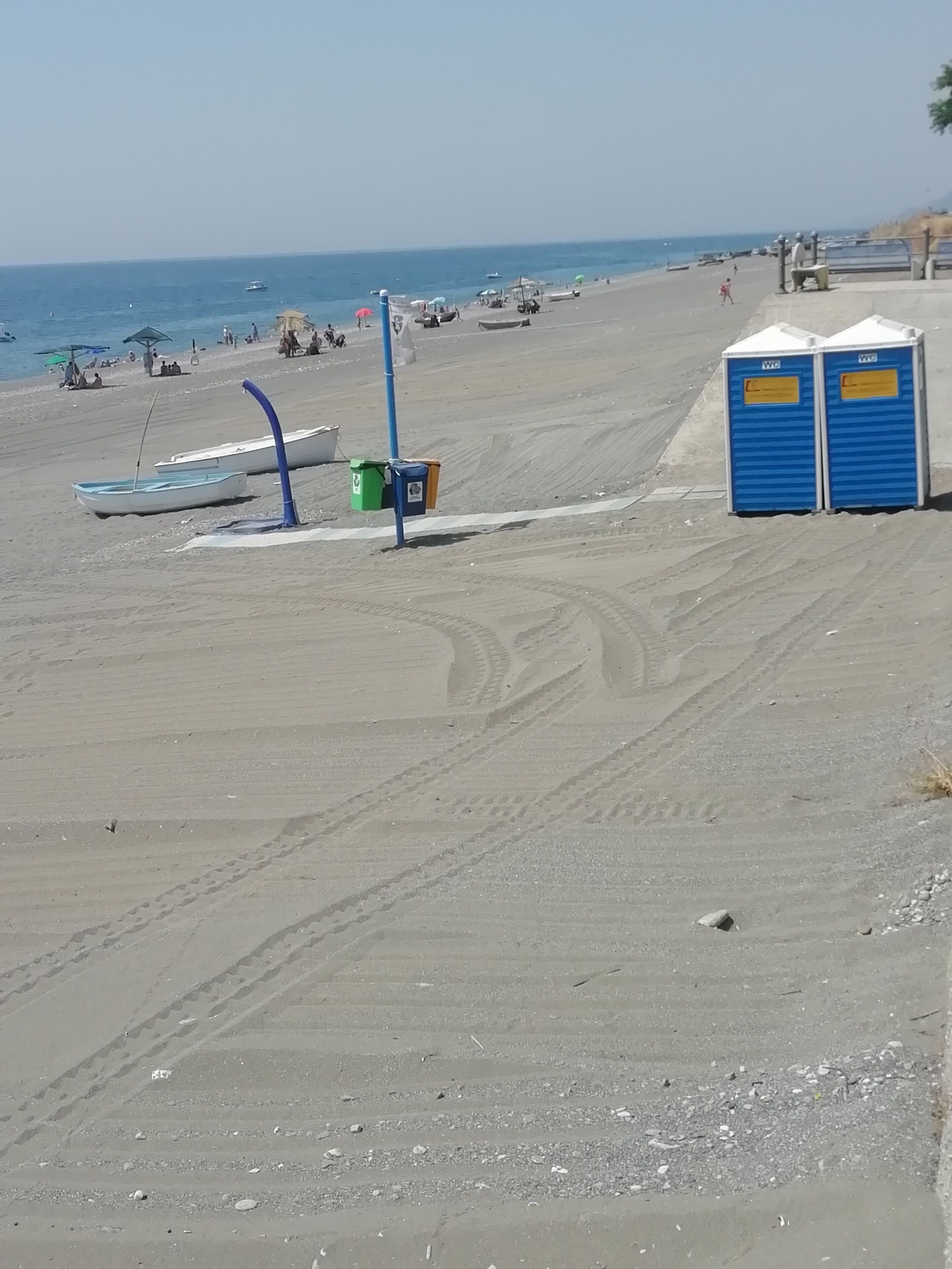 Una playa con baños portátiles, un bote y cielo despejado.