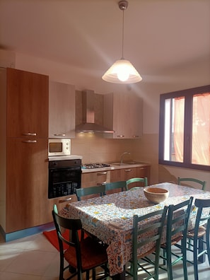 Une cuisine avec des meubles de rangement en bois, un four à micro-ondes, une cuisinière et une table à manger avec des chaises.