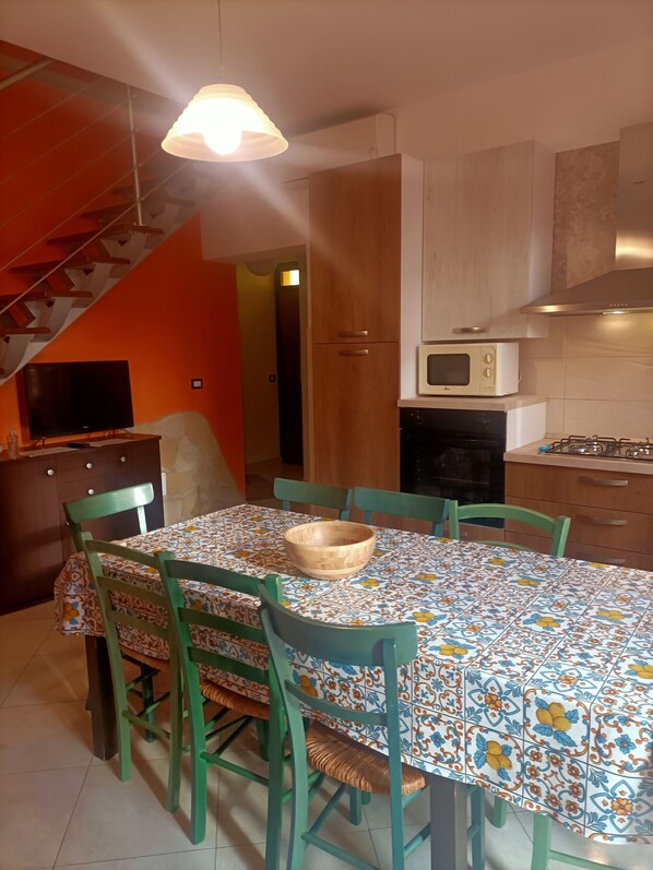 A dining area with a tiled table, green chairs, a wooden bowl, a microwave, and a stove.