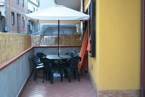 A small outdoor patio with a round table and four chairs, a white umbrella, and a yellow wall.