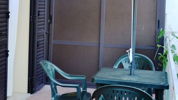 An outdoor patio with a table and chairs, a white umbrella, and a sliding door in the background. - Villetta Singola a 20metri dal Mare per Soggiorni - Cure Termali Vicino Taormina (Ali Terme)