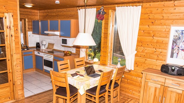 A wooden cabin with a kitchen area featuring a dining table, chairs, and a cabinet. - This is Your House to Stay for Holidays (Oberharz am Brocken)