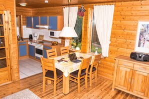 Eine Holzhütte mit Küchenbereich, inklusive Esstisch, Stühlen und einem Schrank.