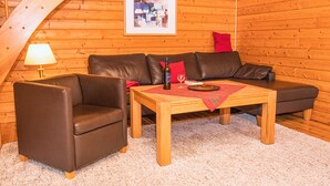 A cozy room with a brown leather sofa, a wooden coffee table, and a small armchair. A framed picture hangs on the wooden wall, and a lamp is on a side table. - This is Your House to Stay for Holidays (Oberharz am Brocken)