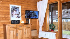 A wooden cabin interior with a wooden cabinet, a television, a radiator, and a window with a curtain. - This is Your House to Stay for Holidays (Oberharz am Brocken)