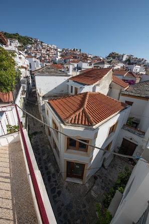 A narrow street with terracotta-tiled buildings, a red railing, and a clear blue sky.