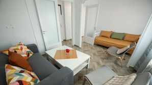 A modern living room with a grey sofa, a white coffee table with a vase, and a brown sofa with orange cushions. - Lovely 1-bedroom Flat In Skopelos (Skopelos)
