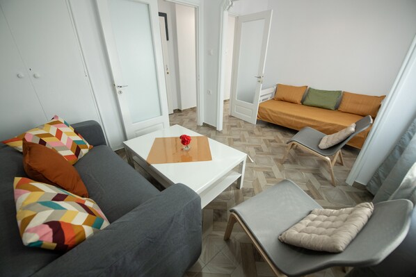 A modern living room with a grey sofa, a white coffee table with a vase, and a brown sofa with orange cushions.