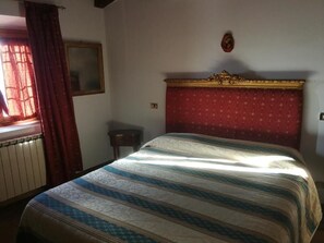 A bedroom with a bed, a window with curtains, a radiator, a mirror, and a wall-mounted decoration. - Room-casetta Verde - Deluxe Room (Vaiano)