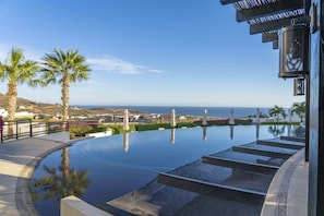 Uma piscina infinita com vista para o oceano, palmeiras e uma estrutura de edifício moderna.