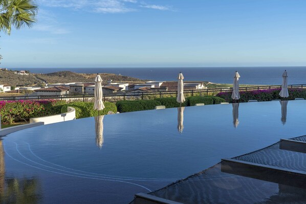 A infinity pool with a view of the ocean and a hillside.