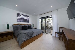 A modern bedroom with a large bed, a wooden nightstand, a bedside table, a TV, and a sliding glass door leading to a balcony.