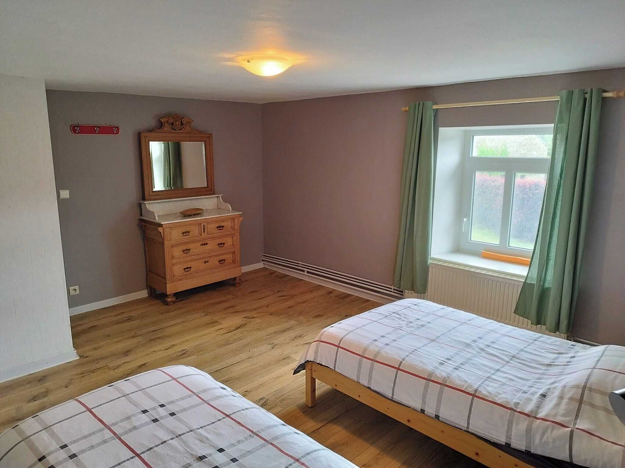 Ein Schlafzimmer mit zwei Einzelbetten, einer Holzkommode, einem Spiegel, einem Fenster mit Vorhängen und einer Lampe.