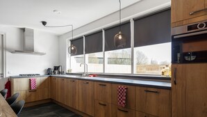 A modern kitchen with wooden cabinets, a large window with blinds, a gas stove, and pendant lighting. - "cozy Luxury Holiday Home With Jacuzzi!" (Heumen)