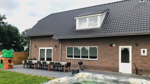 A house with a hot tub, a patio with chairs and a table, and a play structure. - "cozy Luxury Holiday Home With Jacuzzi!" (Heumen)
