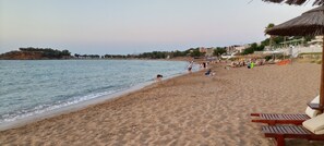 A beach with sand, water, and a few people. There are buildings in the background.