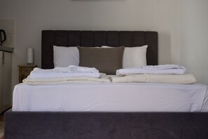 A neatly made bed with white linens and two pillows, a bedside table with a lamp, and a dark headboard.