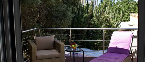 A balcony with a wicker sofa, a small table with fruit, and a sun lounger.