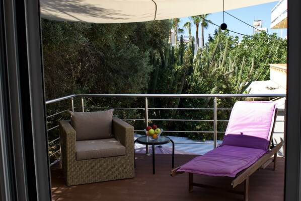 A balcony with a wicker sofa, a small table with fruit, and a sun lounger.