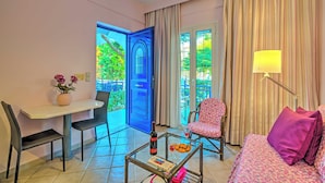 A hotel room with a dining area, a bed, a chair, a table with a bottle and glasses, and a view of greenery outside. - Cozy Apartment Amoudara Heraklion Crera-4 (Malevizi)