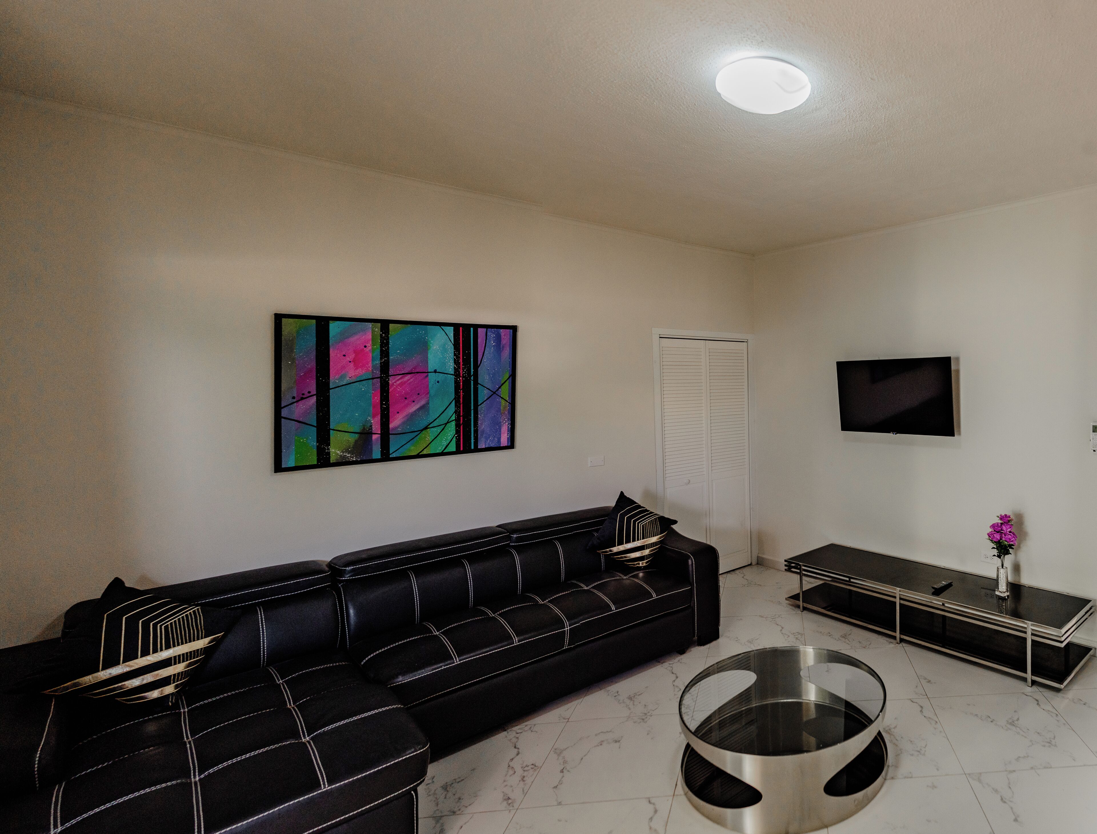 A living room with a black sofa, a glass coffee table, a flat-screen TV, and a colorful abstract painting on the wall.